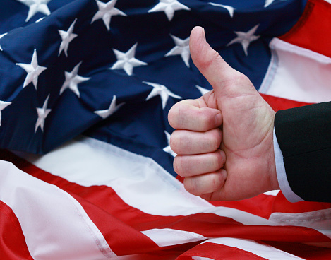 A man giving the thumbs up in front of the American flag, Black dress suit