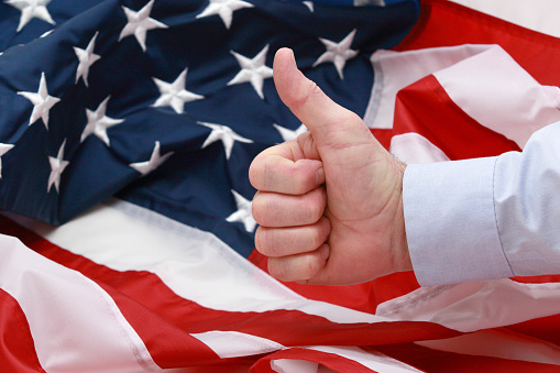 A man giving the thumbs up in front of the American flag, blue dress shirt