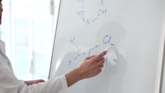 The woman writes a formula on a white board, a close-up