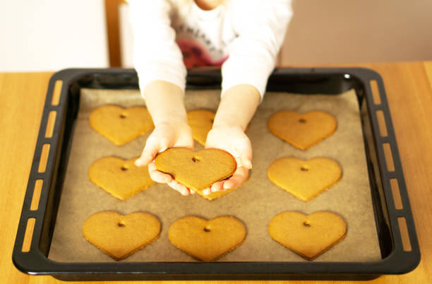 Girl hands with a heart cookie in front of the homemade fresh baked cookies on baking sheet. Valentines Day. High quality photo.