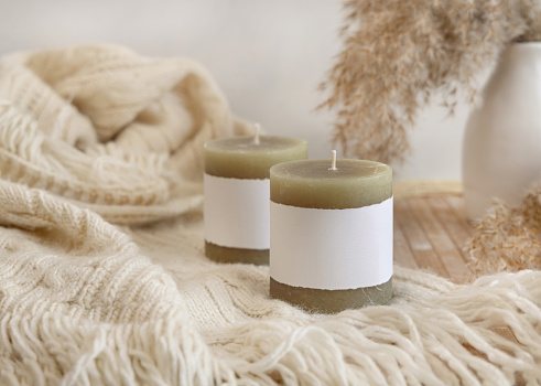 Candles with label on cosy sweater near dry pampas grass Close up, copy space. Boho packaging mock up. Home decorations, Bohemian, ethnic or scandinavian style