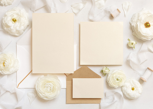 Blank cards  and envelopes near cream roses and white silk ribbons top view, mockup. Romantic scene with wedding set and pastel flowers flat lay. Valentines, Spring or Mothers day concept