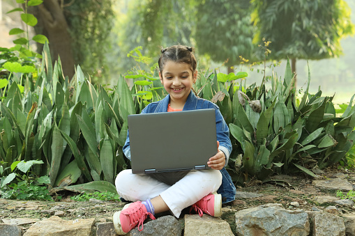 Happy Indian girl working on a Laptop in a lush green park in day time in summer. Busy with work he is a joyous workaholic.