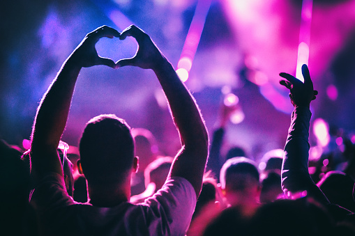 Closeup rear view of group of people at a concert party. One person is showing heart symbol with their hands, released.