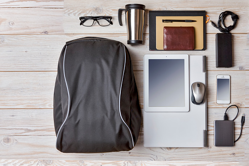 Top View of Backpack With Laptop and Tablet Nearby, Mobile Phone With Notebook and Accessories Over Wooden Background. Concept of Travel Life Accessories
