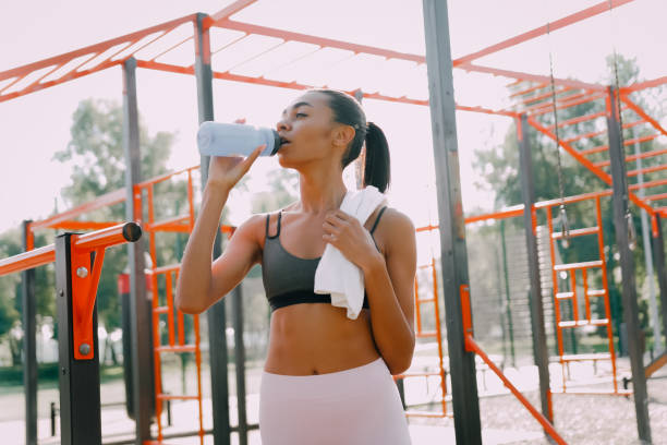 istock Exhausted middle-aged multi ethnic sportswoman with white terry towel drinks water, rests after an evening workout at sunset on the sports ground 1483838917