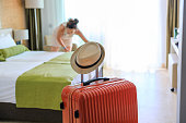 Orange color suitcase delivered in hotel room. Young woman changing bed sheets out of focus