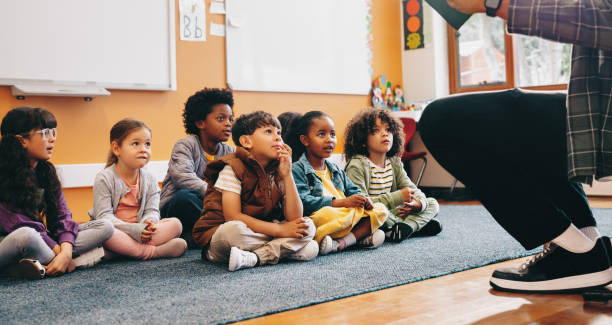 Elementary school students sit and listen to a story from their teacher stock photo