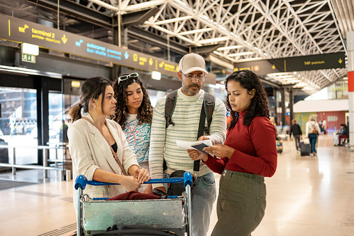 Group of young travelers using smartphone checking flight or online check-in at airport together, with luggage.