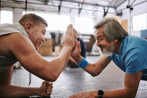Fitness, old men on ground and high five for target, training goals and excited in gym. Senior male athletes, happy elderly citizens and gesture for achievement, exercise or teamwork on ground in gym
