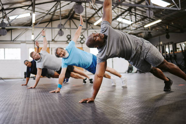 persone, fitness e side plank in classe con personal trainer per allenamento, stretching o allenamento. gruppo eterogeneo in sessione di stretching di riscaldamento con allenatore per il benessere cardio o l'equilibrio sul pavimento - endurance sport foto e immagini stock