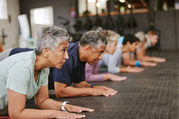 persone, fitness e plank in classe per l'allenamento, l'esercizio di base o l'allenamento insieme nella palestra indoor. gruppo o squadra eterogenea nel riscaldamento ab sessione muscolare per sport, salute o benessere sul pavimento della palestra - endurance sport foto e immagini stock