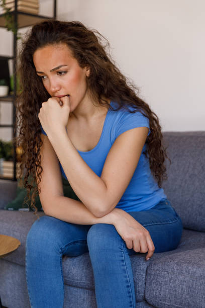 istock Anxious young woman sitting on the sofa, biting her nails, contemplating 1483873653