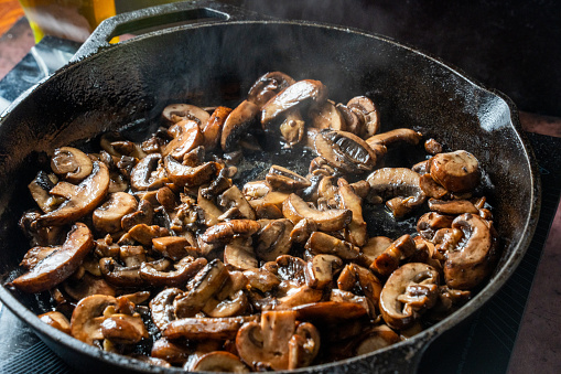Sliced mushrooms being sautéed in butter on a hot cast iron pan, creating a delicious and savory aroma. A perfect side dish or topping for any meal