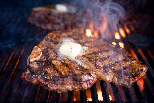 T-bone beef steak cooked to perfection over a flame grill and topped with a dollop of butter is a mouth-watering meal that satisfies any carnivore's cravings stock photo