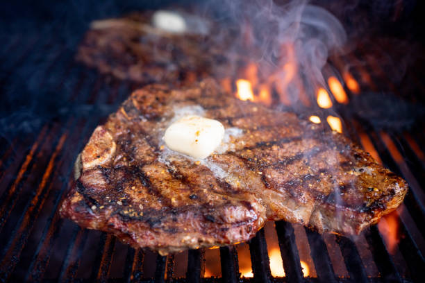 t-bone beef steak cooked to perfection over a flame grill and topped with a dollop of butter is a mouth-watering meal that satisfies any carnivore's cravings - steak red meat beef rib eye steak imagens e fotografias de stock