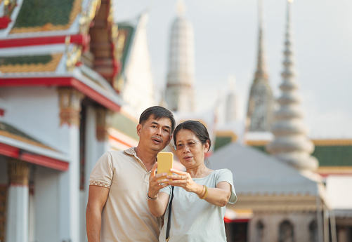 Wide angle Asian senior couple travel feeling amzing with architecure asian culture at Wat Arun temple big landmark in Bangkok Thailand.