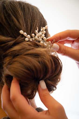 A close up of a hair dressers hands putting the final touches on a brides hair.