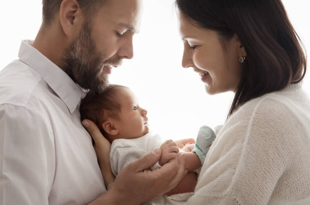 Newborn Family. Happy Parents holding Baby in Hands. Smiling Mother looking at infant Child over White isolated Background. Children Care and Health stock photo