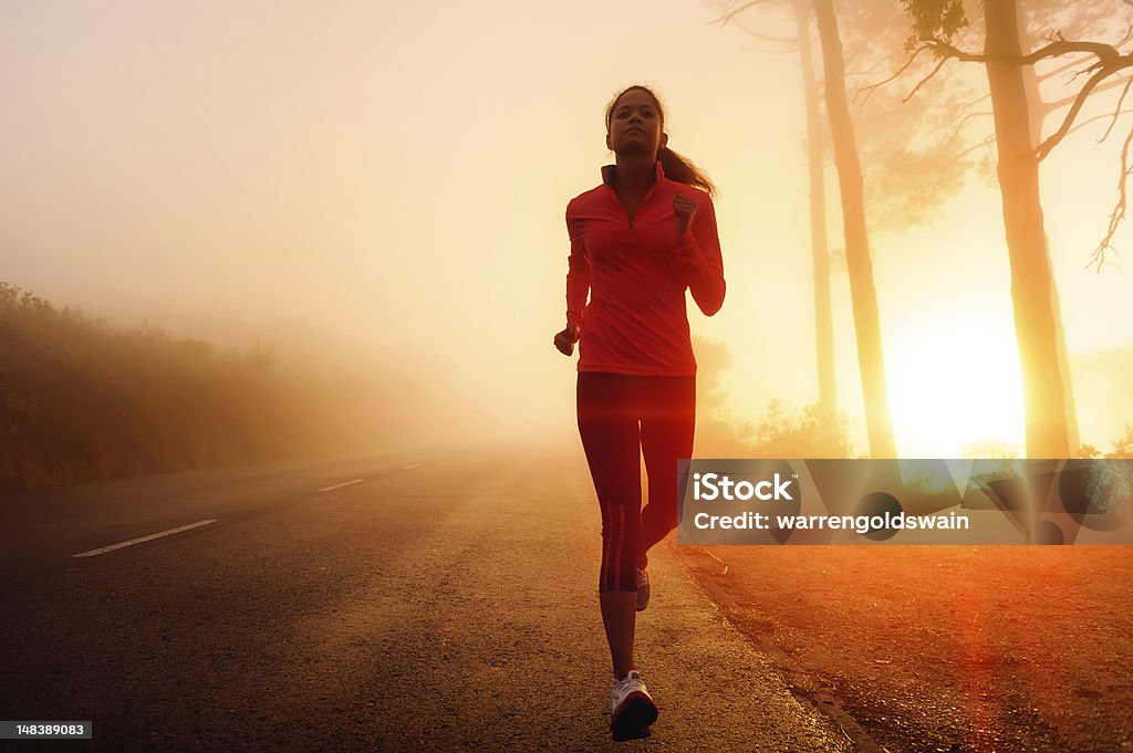 Athlete training Healthy running runner woman early morning sunrise workout on misty mountain road workout jog. sun flare through the mist gives atmospheric feel and depth to these fitness images Active Lifestyle Stock Photo