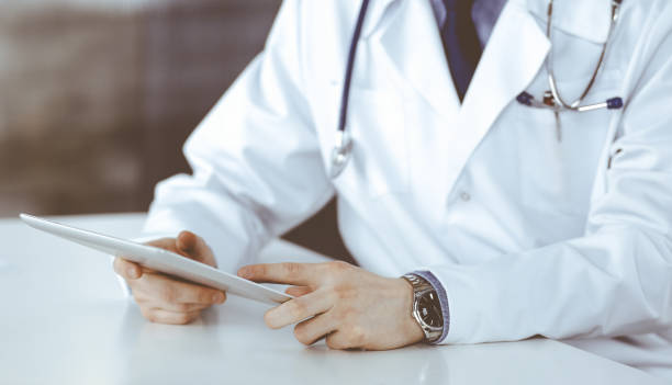 istock Unknown male doctor sitting and working with tablet computer in clinic at his working place, close-up. Young physician at work. Perfect medical service, medicine concept 1483892845