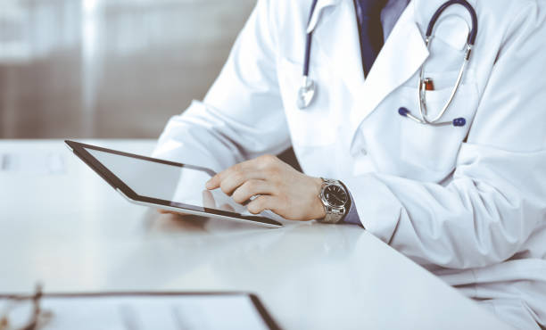 istock Unknown male doctor sitting and working with tablet computer in clinic at his working place, close-up. Young physician at work. Perfect medical service, medicine concept 1483892852