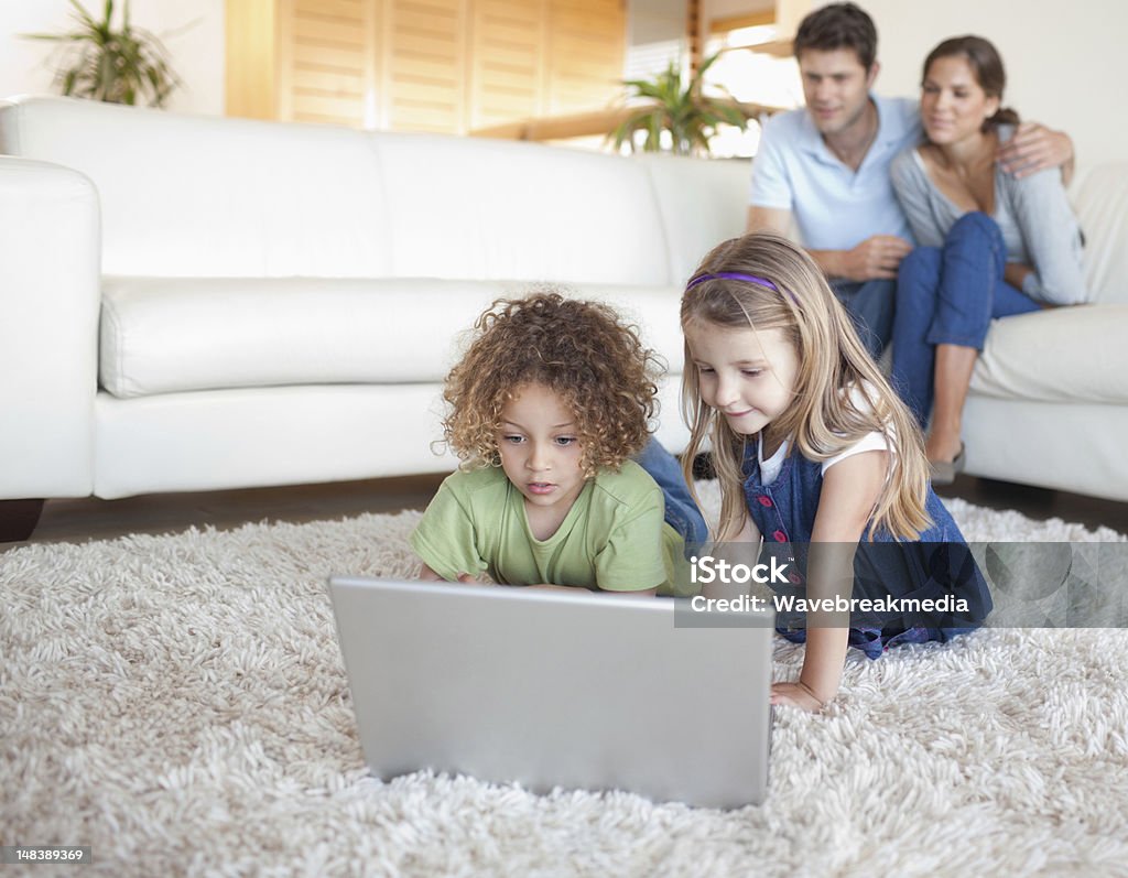 Niños utilizando un cuaderno mientras sus padres están viendo - Foto de stock de 30-39 años libre de derechos