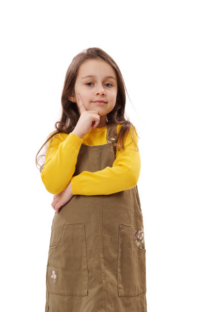 adorable kid girl holding finger on her chin and reasoning seriously, looking at camera, isolated on white background. stock photo