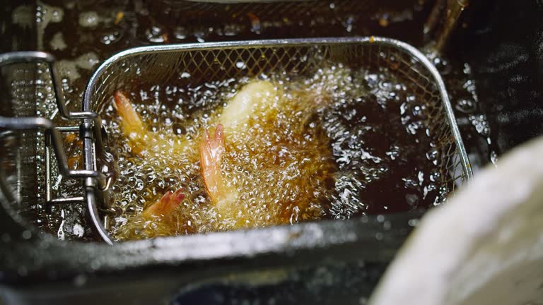 Cooking shrimps in in boiling oil deep fryer at the kitchen. Closeup