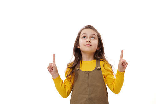 Caucasian little kid girl 5-6 years looking aside up, pointing her index fingers up on copy advertising space over isolated white background. Portrait of clever smart preschooler child, school girl