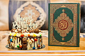 Birthday layer cake decorated with chocolate pieces with happy birthday text with a muslim book with Arabic calligraphy Quran - translation : the noble book of Muslims on wood table