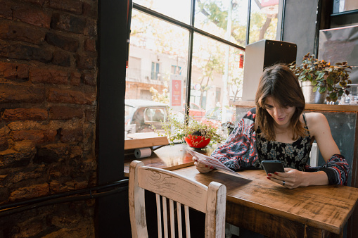 young transgender argentinian ethnicity latina woman sitting in the restaurant using the phone and with the menu in her hand ordering the food, copy space.