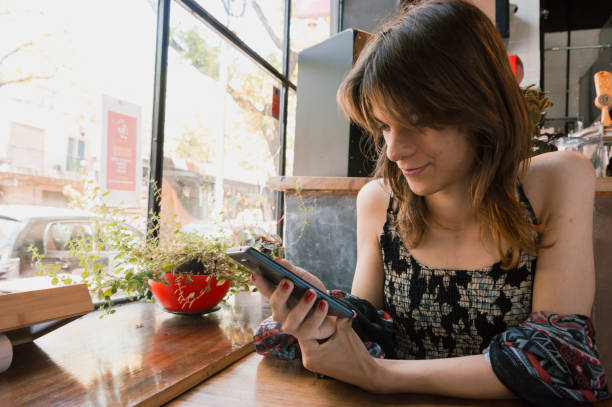 transgender woman alone, sitting using the phone sitting in a restaurant stock photo
