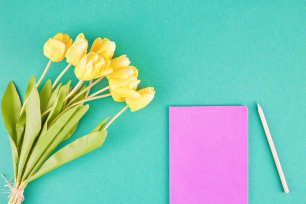 Yellow Tulips, Notebook And Pencil Over Green Background