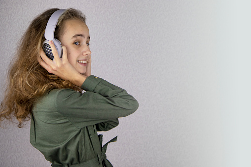 Portrait of a pretty blonde teenage girl listening to music with headphones. She looks at the camera over her shoulder and smiles, enjoys pleasant music and a great mood.