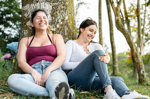 young women sitting on the ground next to a tree, talking and laughing loudly