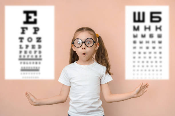 niña sorprendida de 7 años con gafas redondas sobre el fondo de mesas borrosas para comprobar la agudeza visual - eyewear child glasses 6 7 years fotografías e imágenes de stock