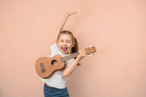 Expressive emotional Caucasian girl of primary school age learns music by playing the children's guitar.