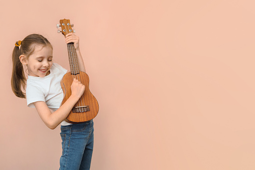 Expressive Caucasian girl of primary school age with a children's guitar or ukulele like a rock star, copy space.