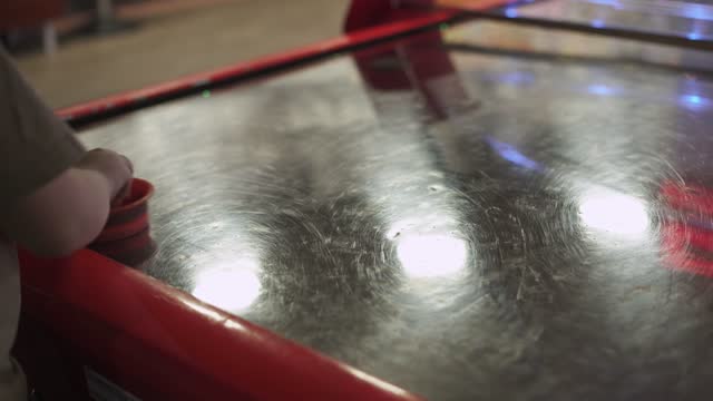 Child hits the puck in air hockey with a plastic bat, close-up.