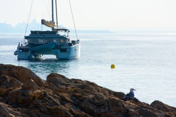 Catamaran anchored off the rocky coast of Ses Illetes with the port of Palma in the background in the mist