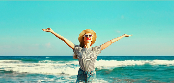 Summer vacation, happy smiling woman raising her hands up on the beach on sea background on sunny day