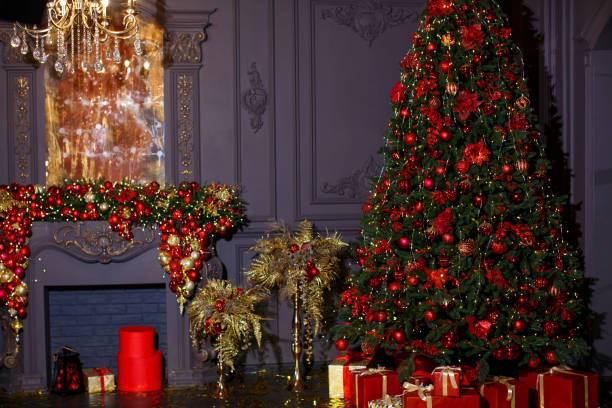 istock A huge Christmas tree with red balls and gift boxes against the backdrop of a fireplace, golden palms and a golden aged mirror 1483919927