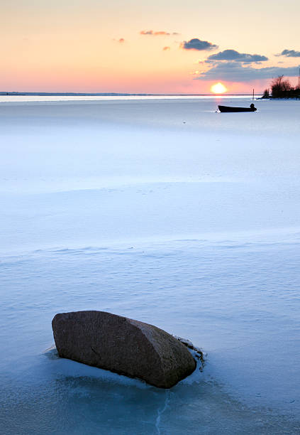 sunset over small bay at the baltic sea, a rock and a boat in the frozen water