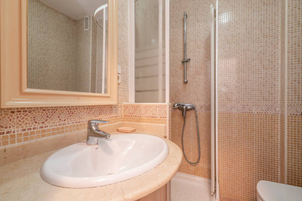 istock Bathroom with small white vanity with cream marble countertop and tiled shower stall with matching valance 1483921269