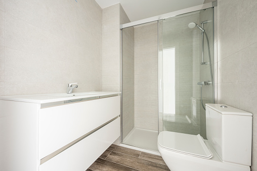 Conventional white wash basin, glass-enclosed shower, tiled floor imitating wood and gray-toned tiles