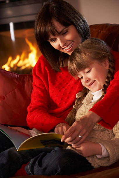 istock Mother And Daughter Sitting On Sofa Reading Book By Fire 148392672