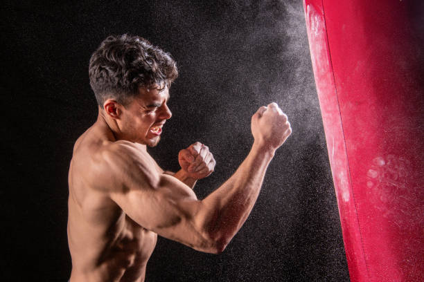 istock Young hispanic athletic man hitting a punching bag on black background 1483927247