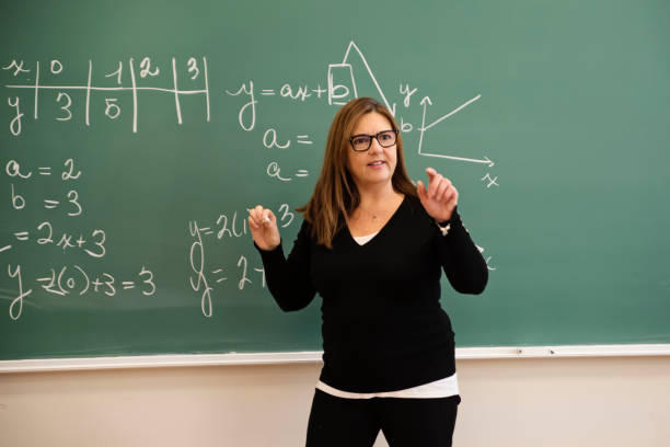 istock Senior female math teacher writing on board in classroom. 1483933697