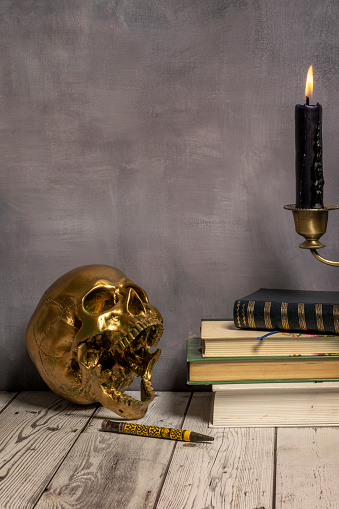 Still life of the reader with a golden skull, a pen and a few books with a candle on top